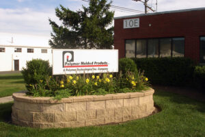 An outside shot of the Polymer Molded Products division which is part of Polymer Technologies Inc. A sign in a bed of flowers states: Polymer Molded Products: A Polymer Technologies Inc. Company with the Polymer logo at the start.