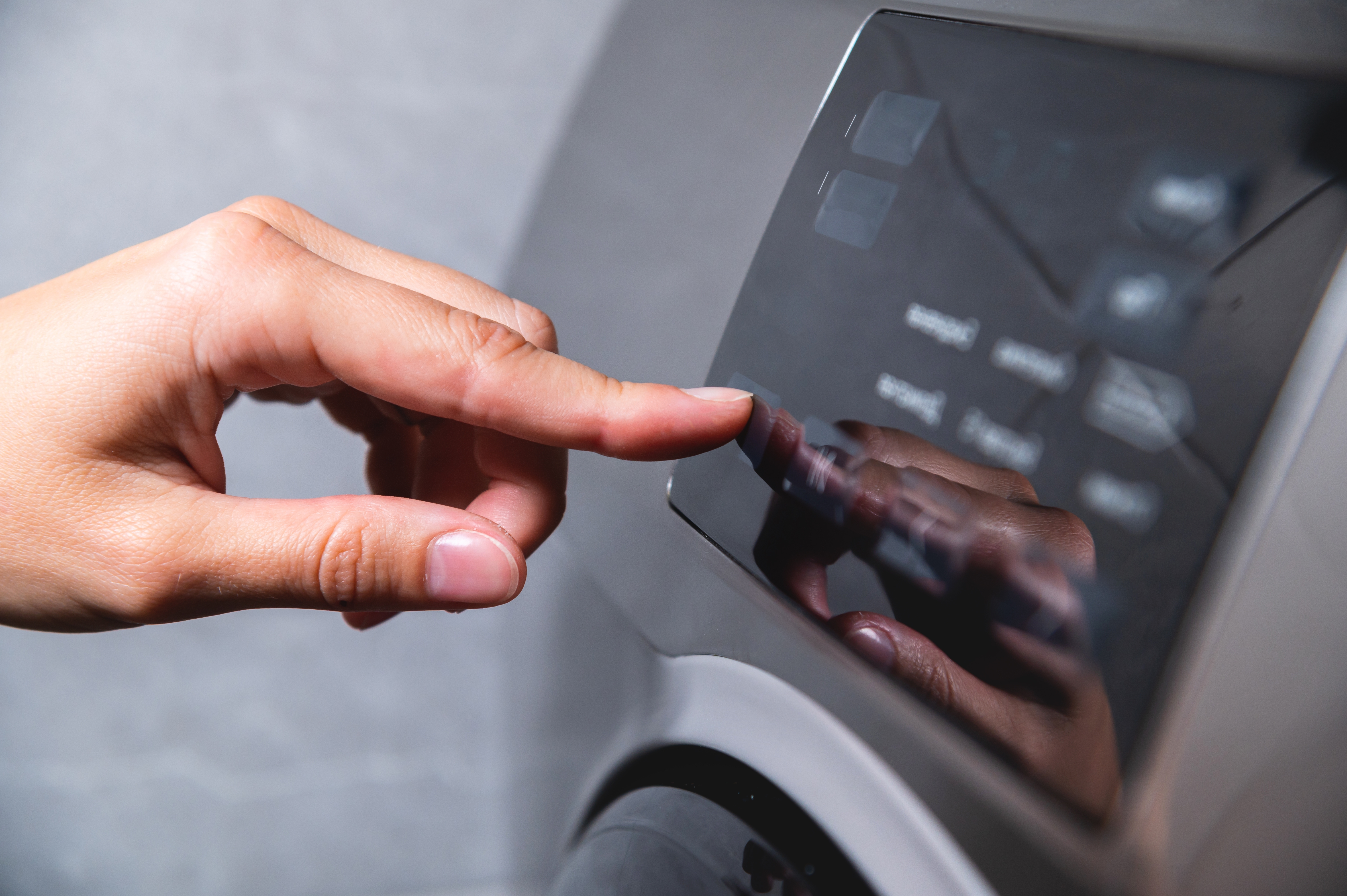 A person's hand shown about to hit start on washing machine.