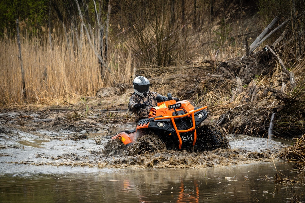 Orange ATV vehicle driving through mud and standing water.